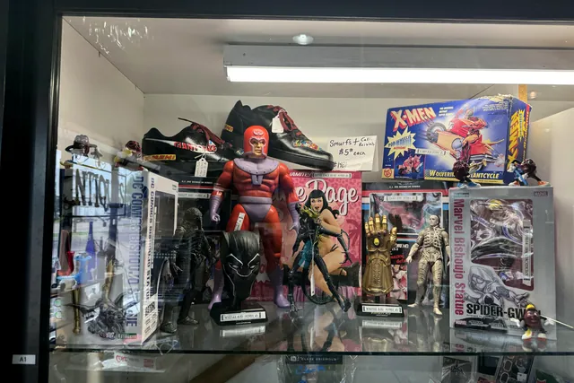 A Deadpool figure, X-Men boxes and an Infinity Gauntlet on a lit glass shelf