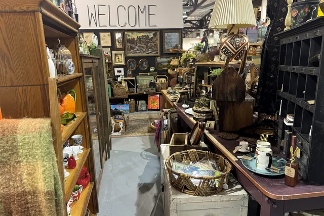 A furnished booth under a Welcome sign, with a dresser, lamp and framed pictures