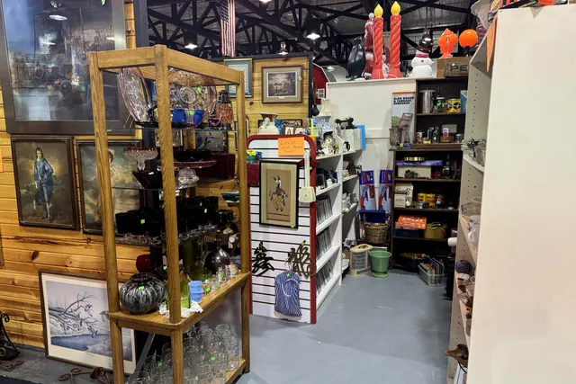 A wooden cabinet and framed pictures beside shelves of glassware
