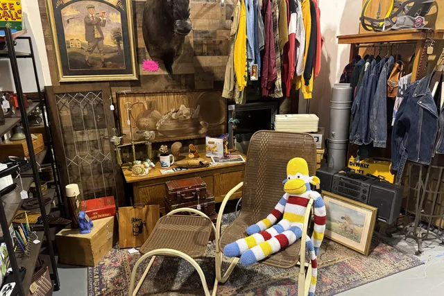 A booth of clothing, framed pictures and oddities around a cane chair