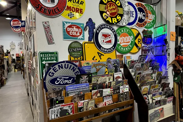 A wall of round porcelain signs, including Double Cola, Buick and Ford, above a rack of old magazines