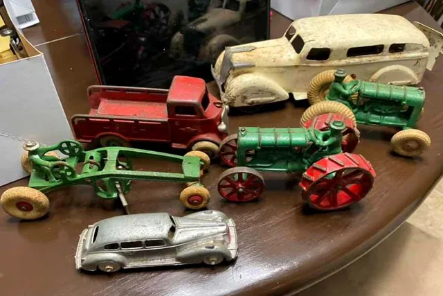 Cast iron toy tractors, a red truck and two cars arranged on a wooden table