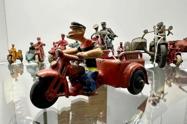 Cast iron toy motorcycles with riders, lined up on a glass shelf