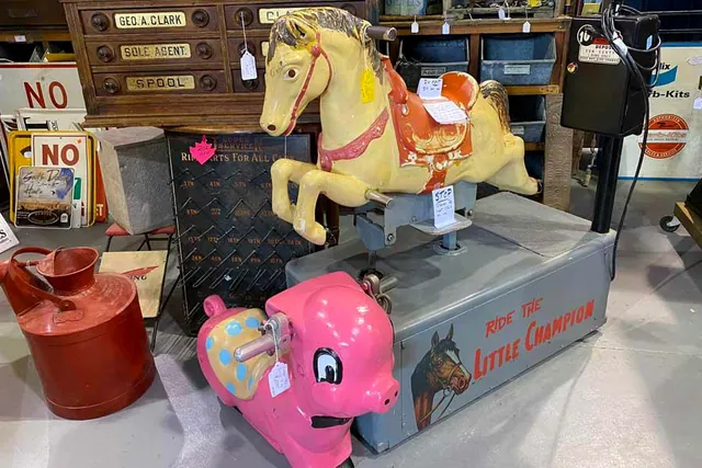 A coin-operated carousel horse ride and a pink pig ride beside an old cabinet